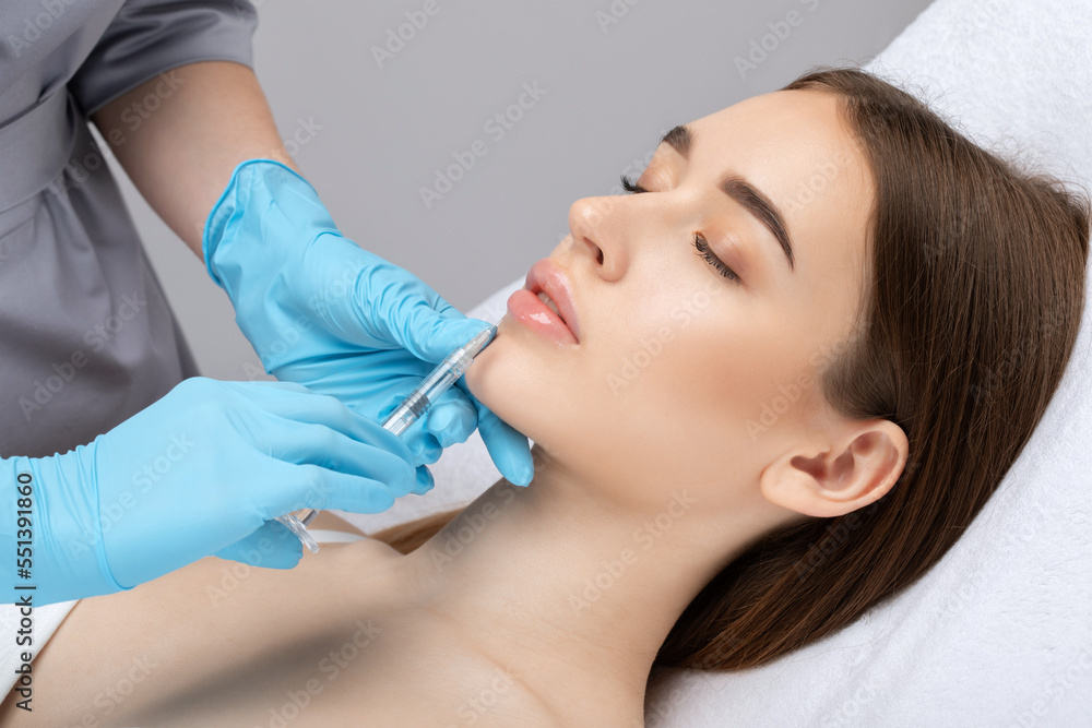 Cosmetologist does injections for lips augmentation and anti wrinkle in the nasolabial folds of a beautiful woman. Women's cosmetology in the beauty salon. Cosmetologist does injections for lips augmentation and anti wrinkle in the nasolabial folds of a beautiful woman. Women's cosmetology in the beauty salon.