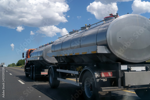 Large truck carrying two tank semi-trailers on country road. Modern truck pulling two white tank trailers with combustible material through countryside in summer