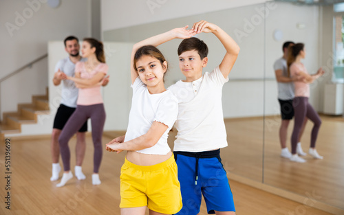 Cute preteen girl and boy siblings enjoying slow foxtrot in pair in dance studio during family training with parents..