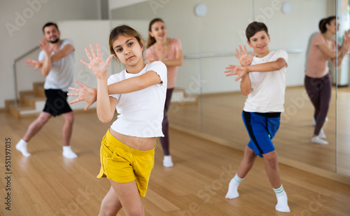 Fototapeta Naklejka Na Ścianę i Meble -  Portrait of positive pre-teen girl doing dance workout with her brother and parents during family class