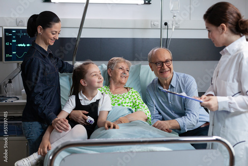 Hospital medical staff member informing elderly female patient family of positive surgical outcome. Healthcare professional checking elderly patient activity in geriatric clinic room.