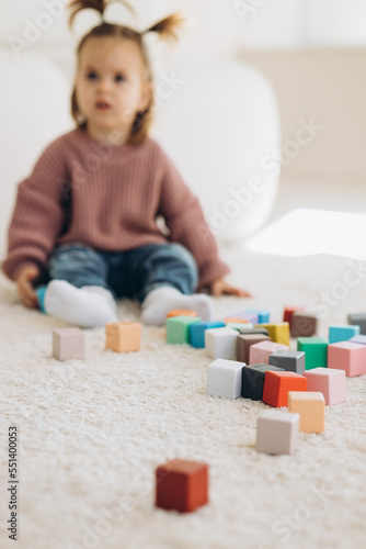 girl plays toys in living room. Montessori wooden toy folded pyramid. Circle, triangle, rectangle wooden elements of children's toys. colored toy blue, yellow, red, green.