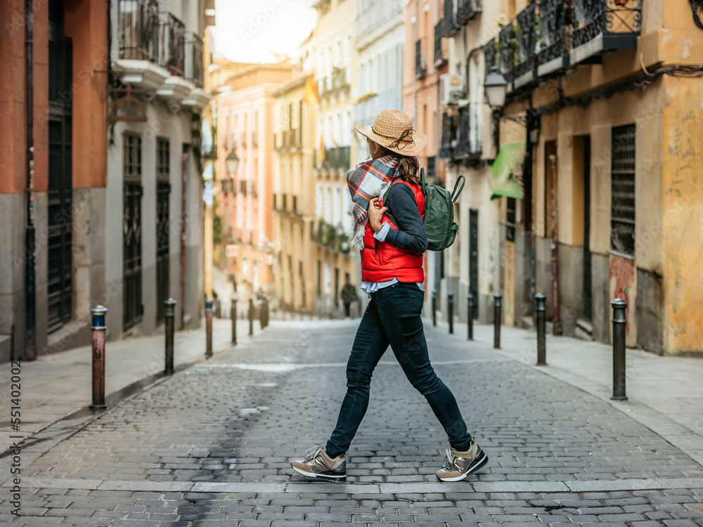 A tourist woman with cap and backpack, crosses a street in the historic center of Madrid. Walking tourism in spain. Concept of tourism and Spanish culture. A tourist woman with cap and backpack, crosses a street in the historic center of Madrid. Walking tourism in spain. Concept of tourism and Spanish culture.