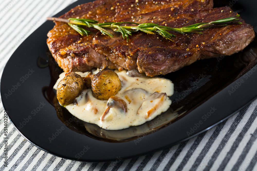 Roasted veal steak with delicious creamy mushroom sauce and rosemary on striped textile surface