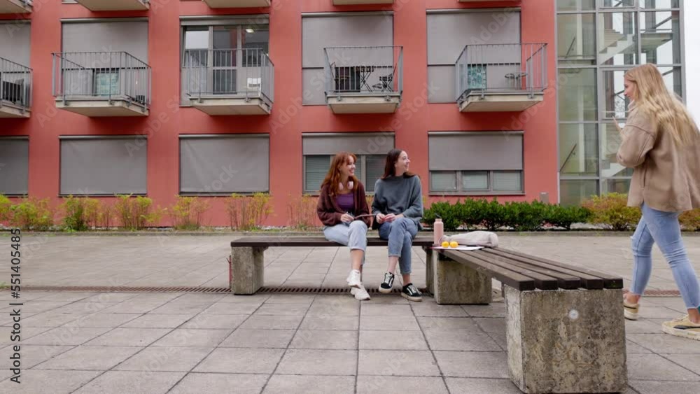 Three college friends meeting outside on a bench in front of the dorm room, one of them arriving late Three college friends meeting outside on a bench in front of the dorm room, one of them arriving late
