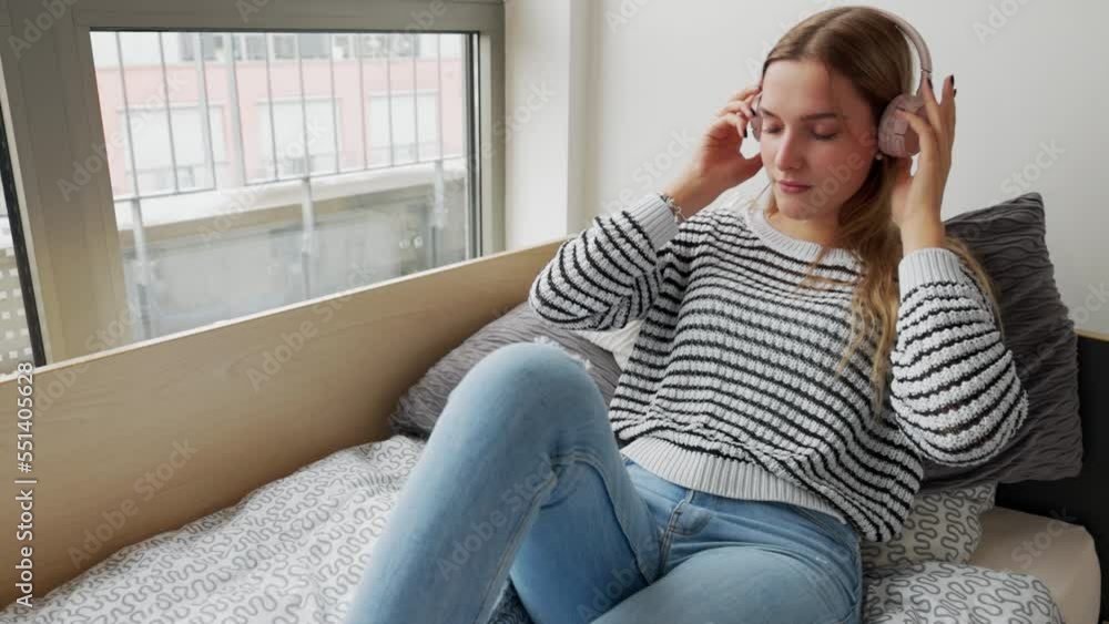 Young college student relaxing in her dorm room listening to some music and reading a book Young college student relaxing in her dorm room listening to some music and reading a book