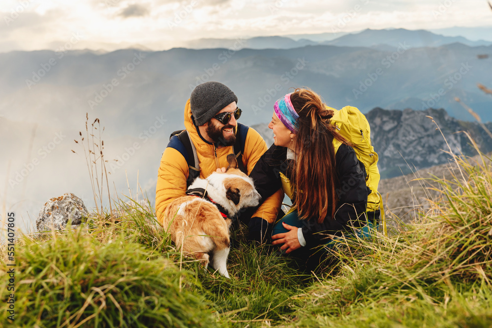 couple of hikers in love, looking into each other's eyes and stroking a dog. A couple doing mountain trekking with her dog. travel with pets