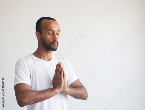 Young afro man concentrating his mind, keeping hands namaste gesture, meditating, yoga exercise breath technique reduce stress.