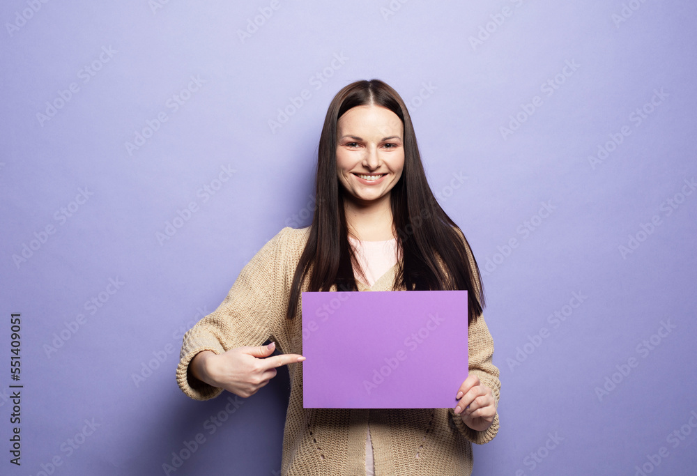 Young woman holding purple blank advertising board standing on lilac background in studio Young woman holding purple blank advertising board standing on lilac background in studio