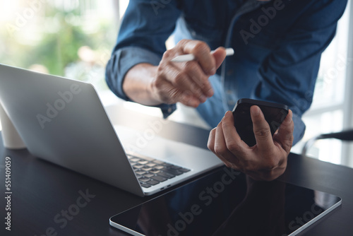 Multitasking businessman using mobile phone, working on laptop computer with digital tablet on office table