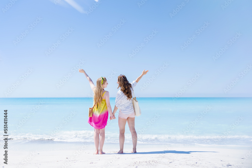 Seen from behind mother and teenage daughter at beach rejoicing