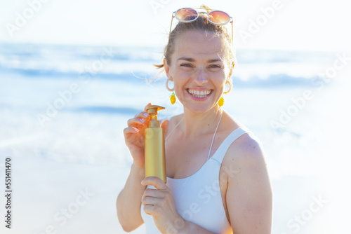 Portrait of happy elegant woman in beachwear at beach using spf © Alliance