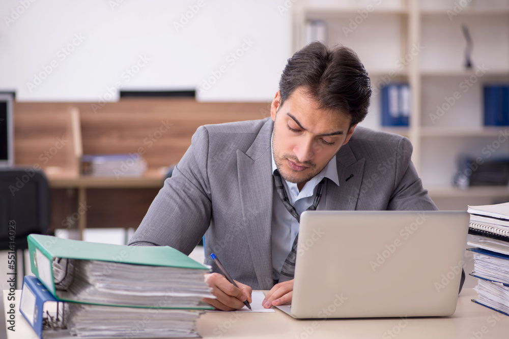 Young male employee unhappy with excessive work in the office Young male employee unhappy with excessive work in the office