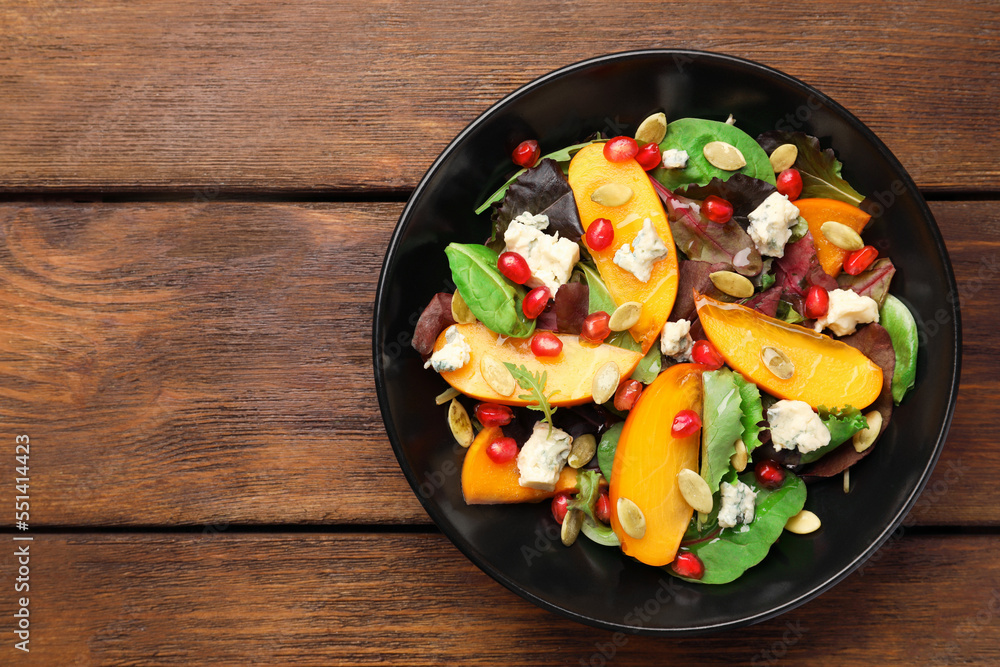 Delicious persimmon salad with pomegranate and spinach on wooden table, top view. Space for text Delicious persimmon salad with pomegranate and spinach on wooden table, top view. Space for text
