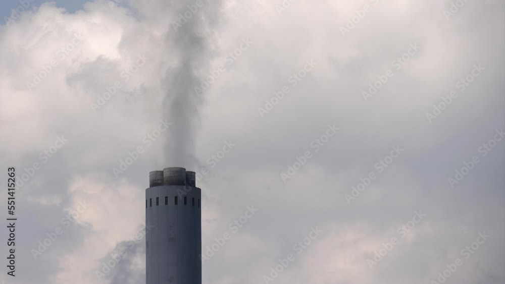 Single tall industrial smoke stack chimney pours smoke into cloudy sky Single tall industrial smoke stack chimney pours smoke into cloudy sky