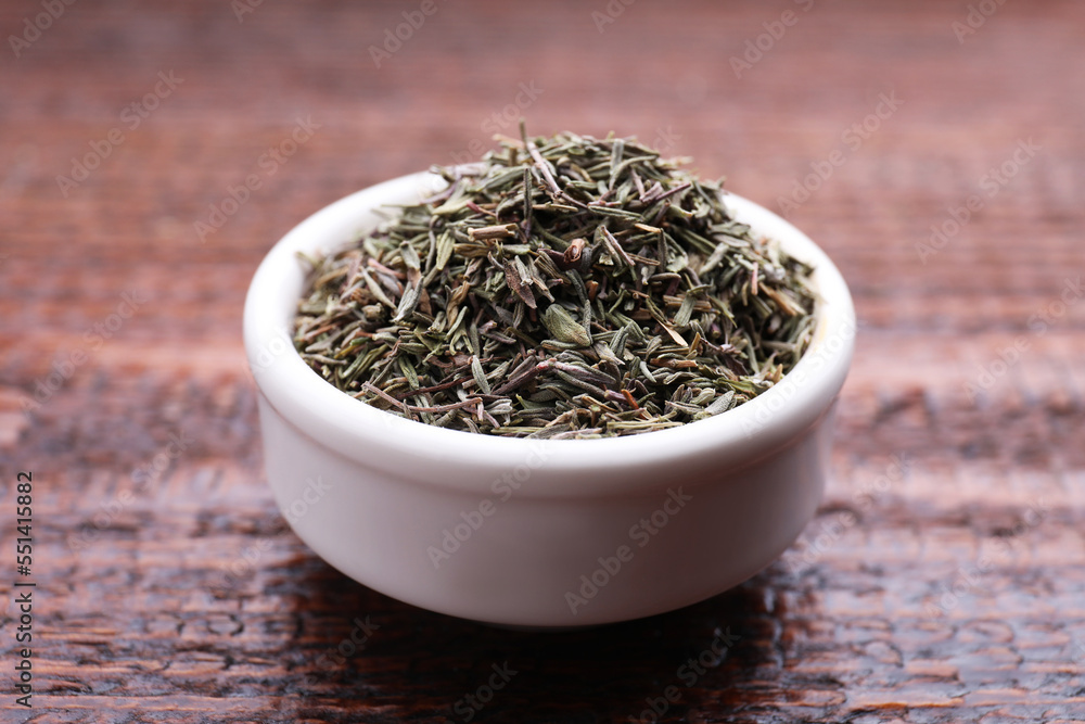 Bowl with dried thyme on wooden table, closeup