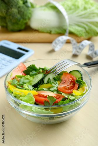 Calculator  tasty salad in bowl and other food on wooden table. Weight loss concept