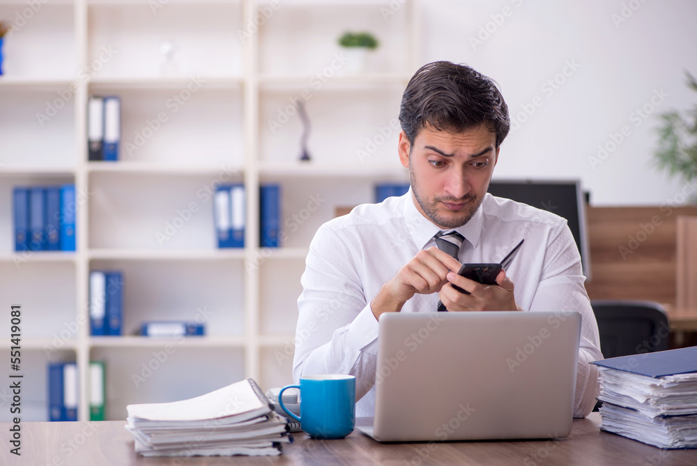 Young male employee unhappy with excessive work at workplace Young male employee unhappy with excessive work at workplace