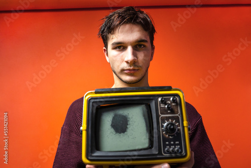 Young man with messy hair marginal look old vintage broken TV zombified passive look on a red background. Activist youth against fake false news TV propaganda. Zombie fake news. Addicted man  photo