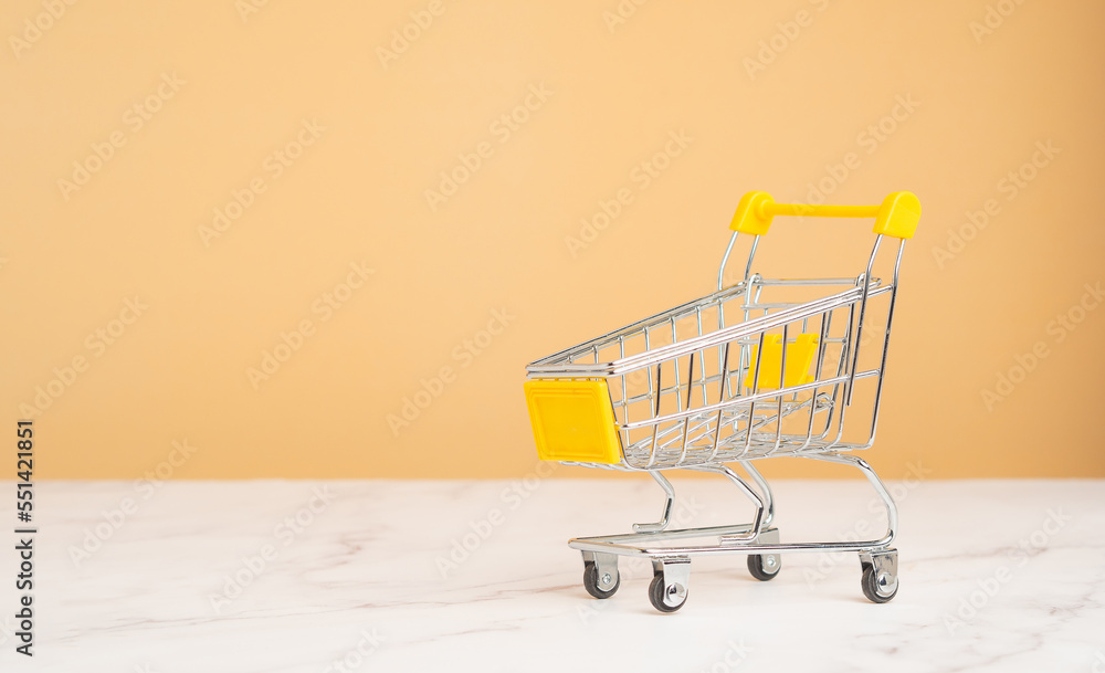 An empty mini shopping trolley on a marble table with an orange background