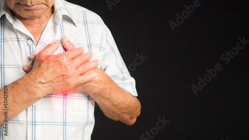 Senior man is suffering from chest pain while standing on a black background © meeboonstudio