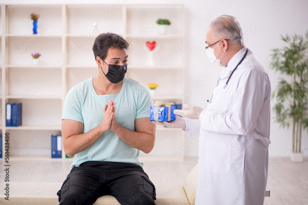 Old male doctor giving giftbox to young male patient Old male doctor giving giftbox to young male patient
