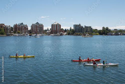 Kayakers on the ocean near a port city with seaplane, boats, and floating homes. © Alain Bechard