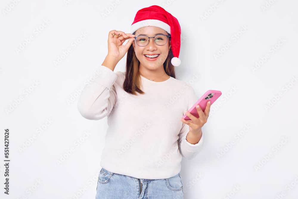 Smiling young Asian woman in a Christmas hat holding smartphone getting great news isolated over white background. celebration Christmas holiday and New Year concept Smiling young Asian woman in a Christmas hat holding smartphone getting great news isolated over white background. celebration Christmas holiday and New Year concept