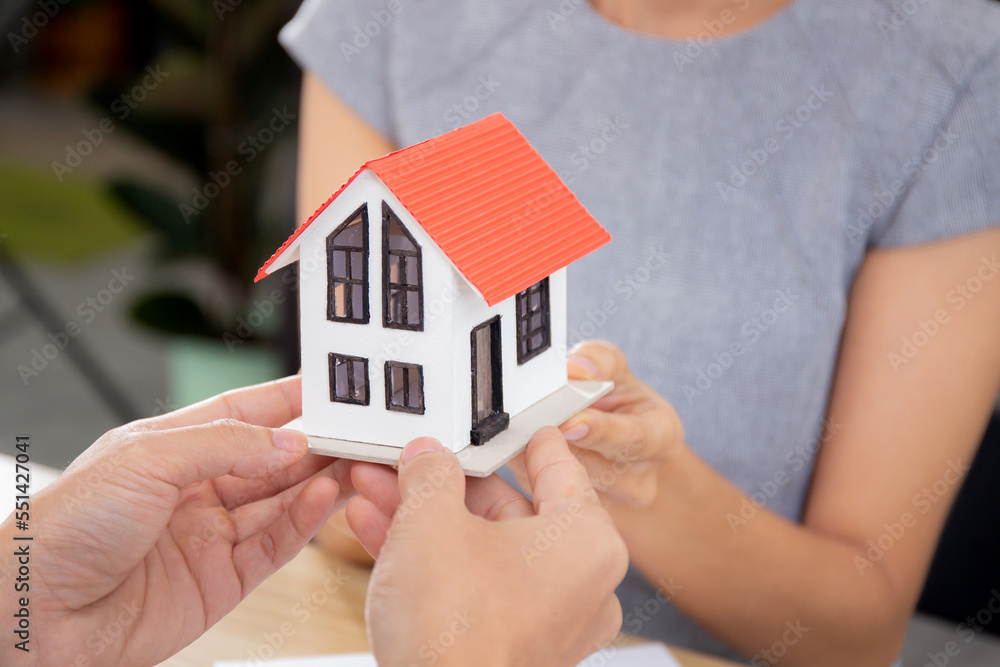 Closeup hands of young realtor man real estate giving house model to hands customer while agreement and contract achievement and approval at home office, investment and mortgage, business concept. Closeup hands of young realtor man real estate giving house model to hands customer while agreement and contract achievement and approval at home office, investment and mortgage, business concept.