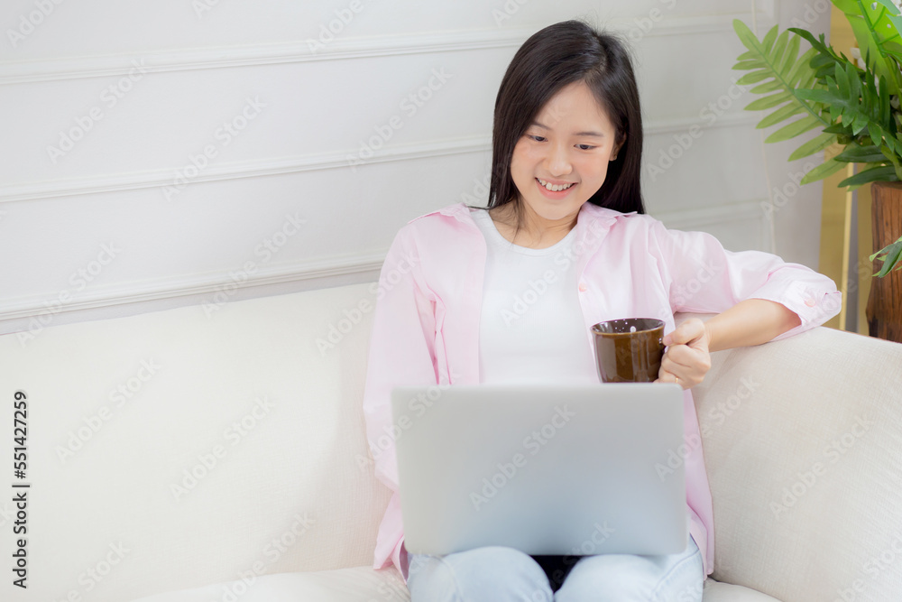 Young asian business woman work from home with laptop computer and drinking coffee on sofa in living room, freelance girl using notebook sitting on couch with comfort and relax, lifestyles concept. Young asian business woman work from home with laptop computer and drinking coffee on sofa in living room, freelance girl using notebook sitting on couch with comfort and relax, lifestyles concept.
