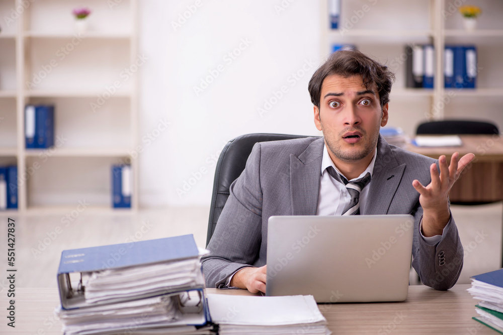 Young male employee unhappy with excessive work in the office Young male employee unhappy with excessive work in the office