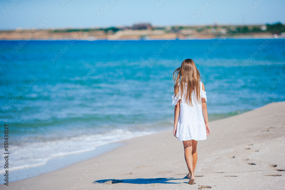 Back view of adorable little girl with long hair in white dress walking on tropical beach vacation Back view of adorable little girl with long hair in white dress walking on tropical beach vacation