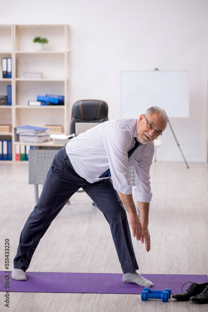Old male employee doing sport exercises at workplace