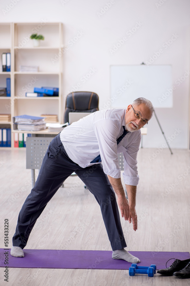 Old male employee doing sport exercises at workplace Old male employee doing sport exercises at workplace
