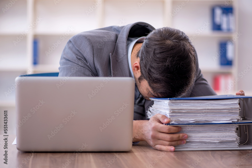 Young male employee unhappy with excessive work in the office Young male employee unhappy with excessive work in the office