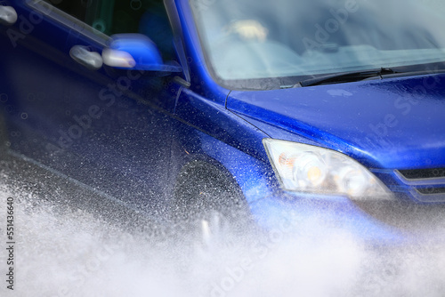 Фотография car is driving through a puddle splashes rain downpour
