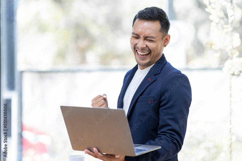 Happy excited Asian man holding laptop and raising his arm up to celebrate success or achievement. Happy excited Asian man holding laptop and raising his arm up to celebrate success or achievement.