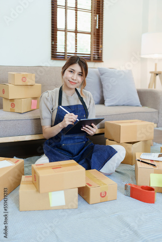 Starting small business entrepreneur of independent young Asian woman online seller is using smart phone and taking orders to pack products for delivery to customers. SME delivery concept © Jirapong