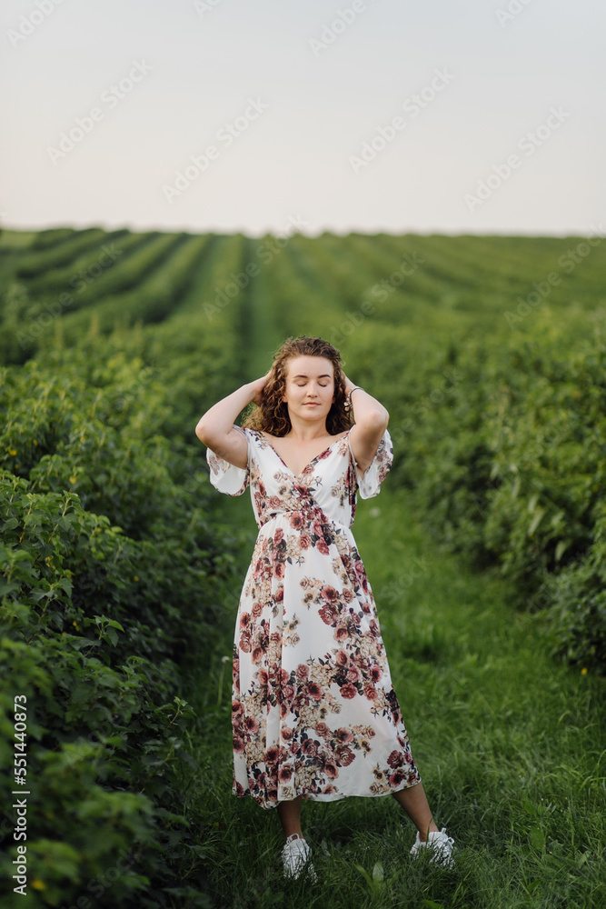 Happy young woman with brown curly hair, wearing a dress, posing outdoors in a garden Happy young woman with brown curly hair, wearing a dress, posing outdoors in a garden