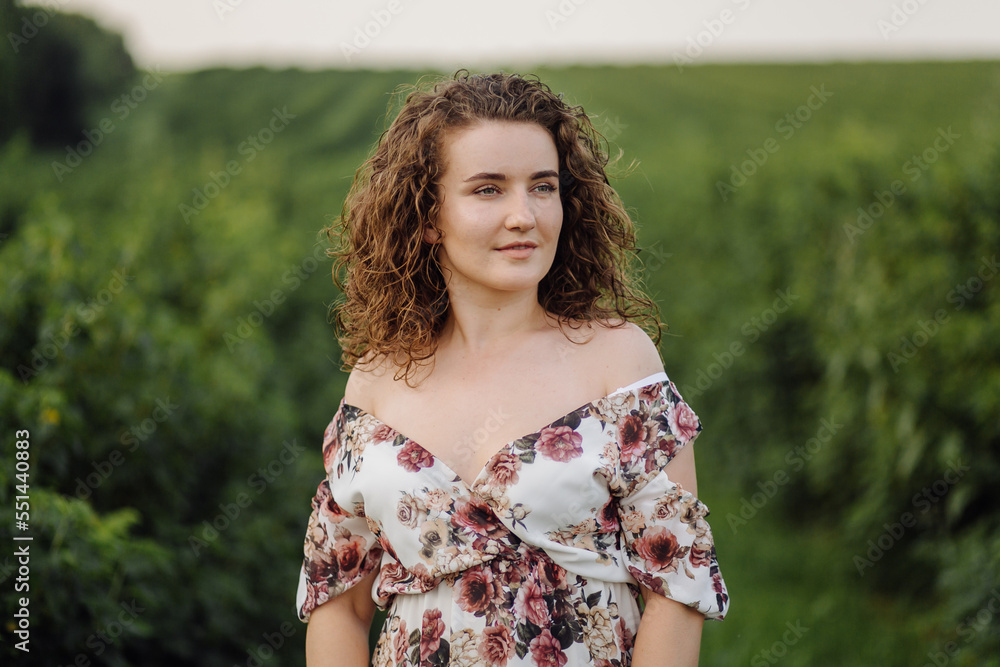 Happy young woman with brown curly hair, wearing a dress, posing outdoors in a garden Happy young woman with brown curly hair, wearing a dress, posing outdoors in a garden