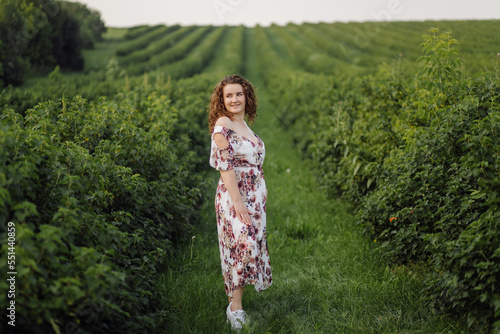 Happy young woman with brown curly hair  wearing a dress  posing outdoors in a garden