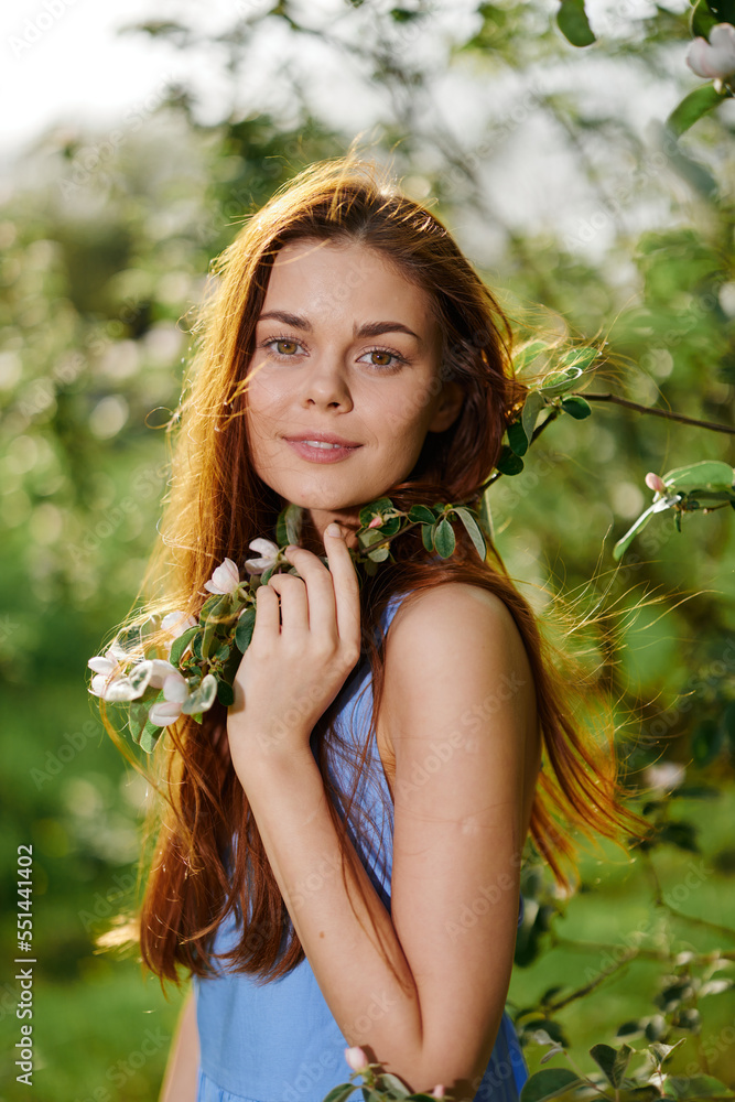 Beautiful woman smile with teeth with long red hair near a tree in the summer sun in nature in the park smiling without allergies in a blue dress, the concept of health and beauty Beautiful woman smile with teeth with long red hair near a tree in the summer sun in nature in the park smiling without allergies in a blue dress, the concept of health and beauty