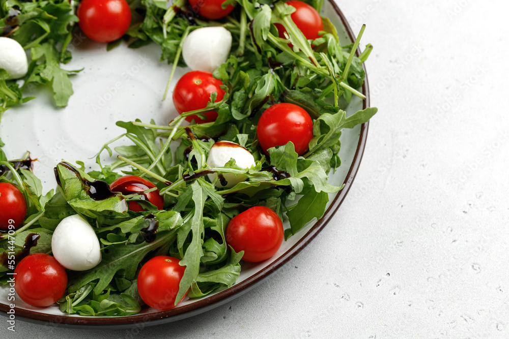 Salad with arugula, cherry tomatoes and mozzarella cheese on round plate and gray background. Salad with arugula, cherry tomatoes and mozzarella cheese on round plate and gray background.