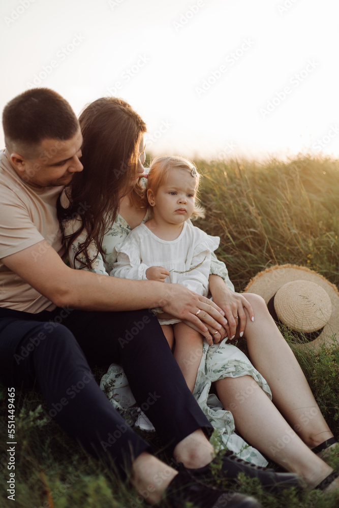 Beautiful caucasian family of father, mother and little daughter posing on camera on background of green field Beautiful caucasian family of father, mother and little daughter posing on camera on background of green field