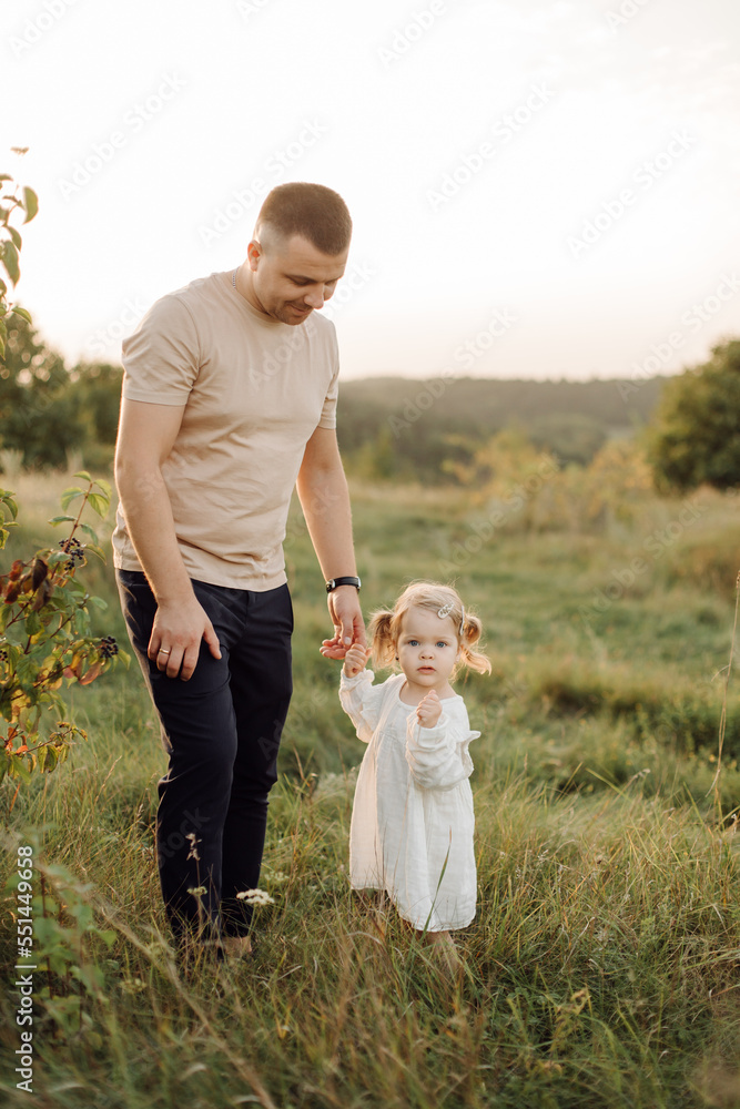 Fototapeta premium Beautiful caucasian family of father, mother and little daughter posing on camera on background of green field