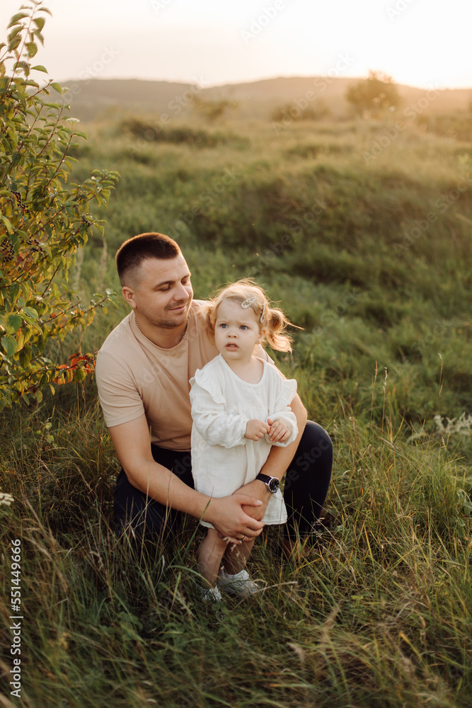 Beautiful caucasian family of father, mother and little daughter posing on camera on background of green field Beautiful caucasian family of father, mother and little daughter posing on camera on background of green field