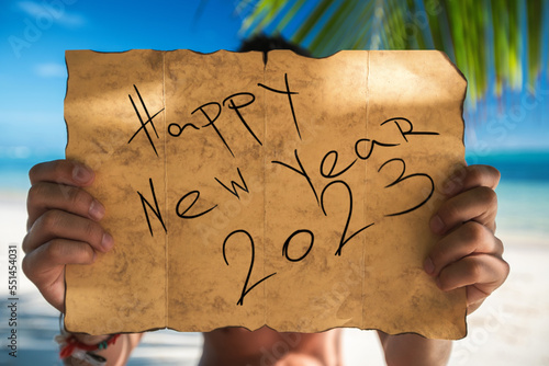 Fototapeta Naklejka Na Ścianę i Meble -  2023 Happy new year travel and lifestyle concept with map and tourist man on tropical island beach. Banner for winter, summer exotic family vacation.