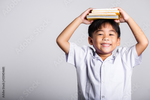 Asian adorable toddler smiling happy wear student thai uniform red pants stand holding book over head and screaming in studio shot isolated on white background, Portrait little children boy preschool