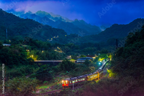 At night, a train with lights moves through the forest in the mountains. A small train station in the mountain forest.. Wanggu Railway Station, Pingxi District, New Taipei City. Taiwan photo
