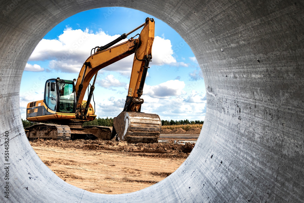 Powerful excavator at the construction site. View of the excavator through the pipe. Close-up of earthmoving machinery. Construction equipment for earthworks. Soil development.